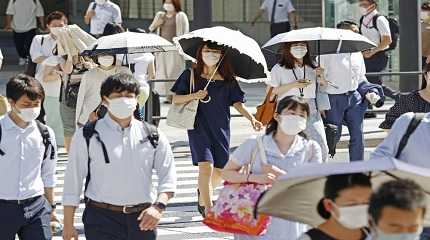 People, some of them holding parasols, cross an intersection amid heat