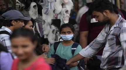 People walk past a girl wearing a face mask