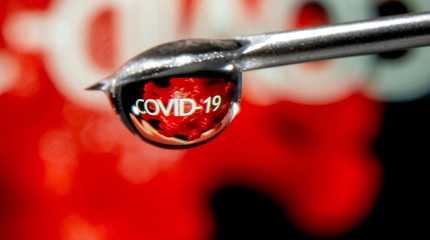 The word "COVID-19" is reflected in a drop on a syringe needle