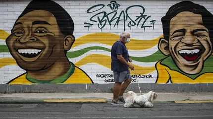 man walks his dog past a mural of Brazilian soccer stars Pele