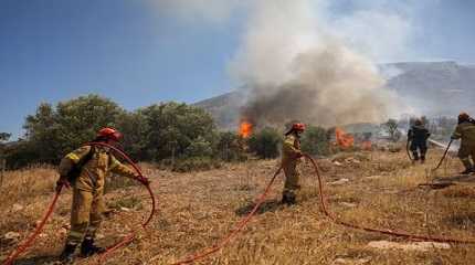 Firefighters try to extinguish a wildfire burning in Kouvaras