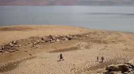 family walks over cracked mud near Lake Oroville's shore