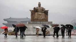 Pedestrians wearing masks walk with umbrellas