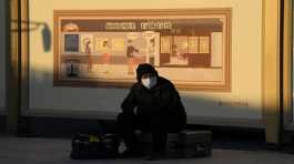 man wearing a mask sits on his luggage