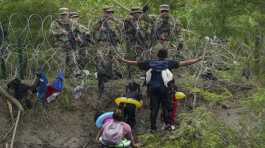 migrant gestures to Texas National Guards standing behind razor wire 